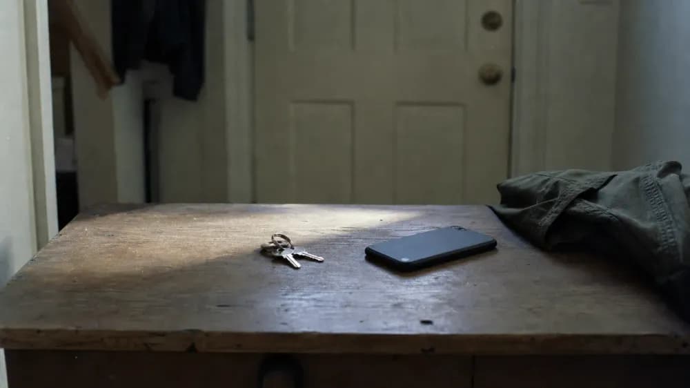 A set of car keys and a phone lying on a worn wooden hall table beside a front door in flat early morning light.