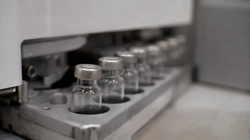 A row of small clear glass vials standing in a metal autosampler tray on a laboratory instrument, photographed close up with the background out of focus.