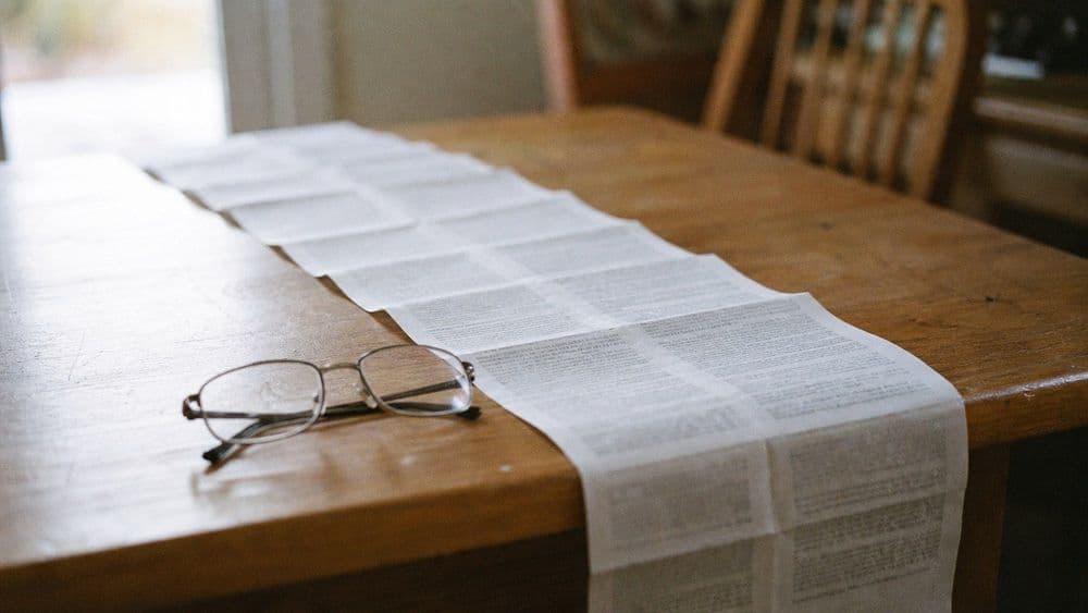 A long folded paper medication insert opened flat on a kitchen table in daylight, its dense small print blurred beyond legibility.