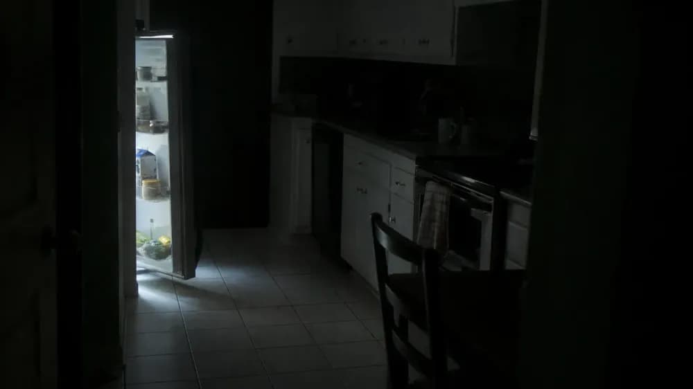 A dark home kitchen at night lit only by the open refrigerator, with nobody in the frame.